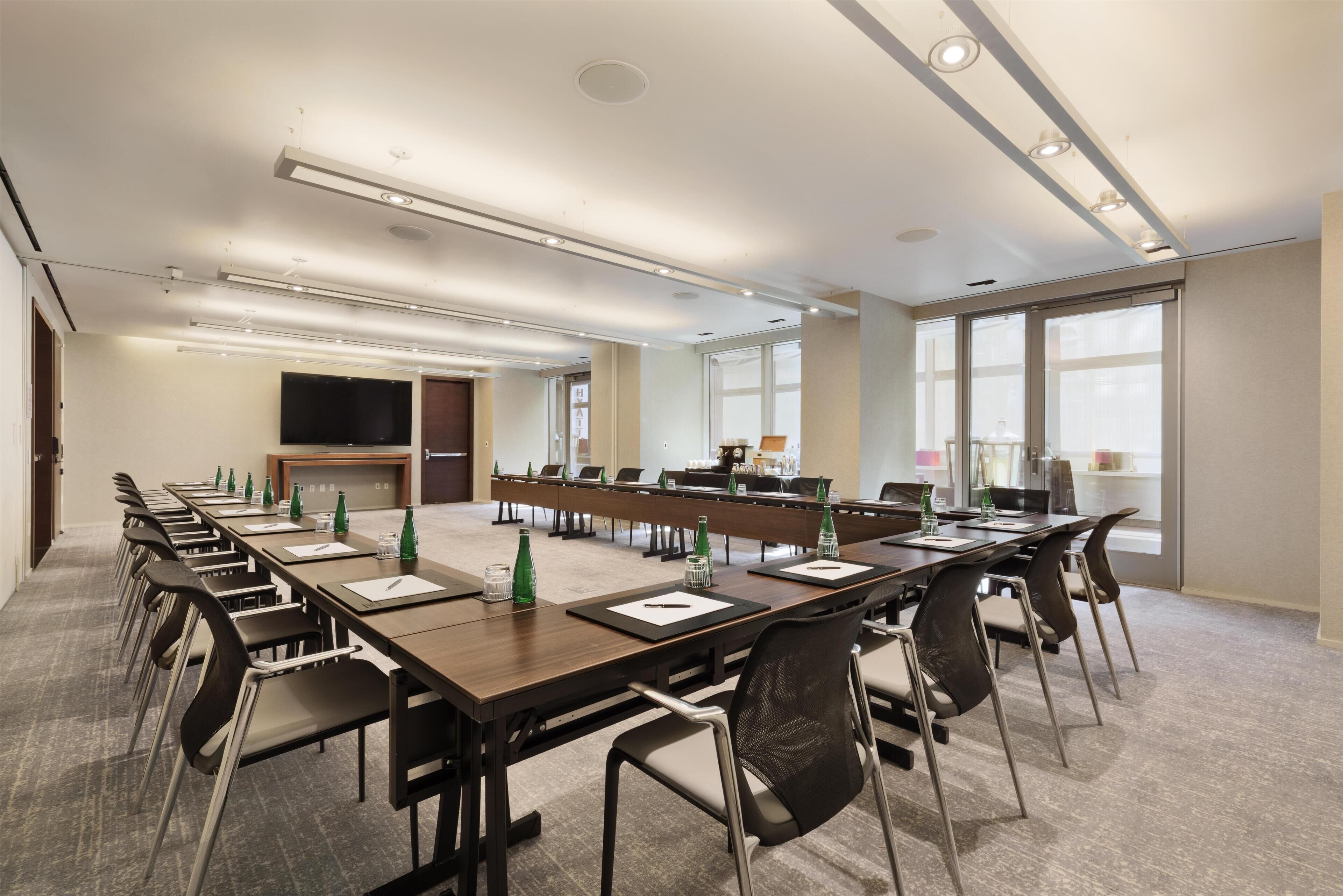 A conference room with long tables, chairs, a flat-screen TV, and large windows.
