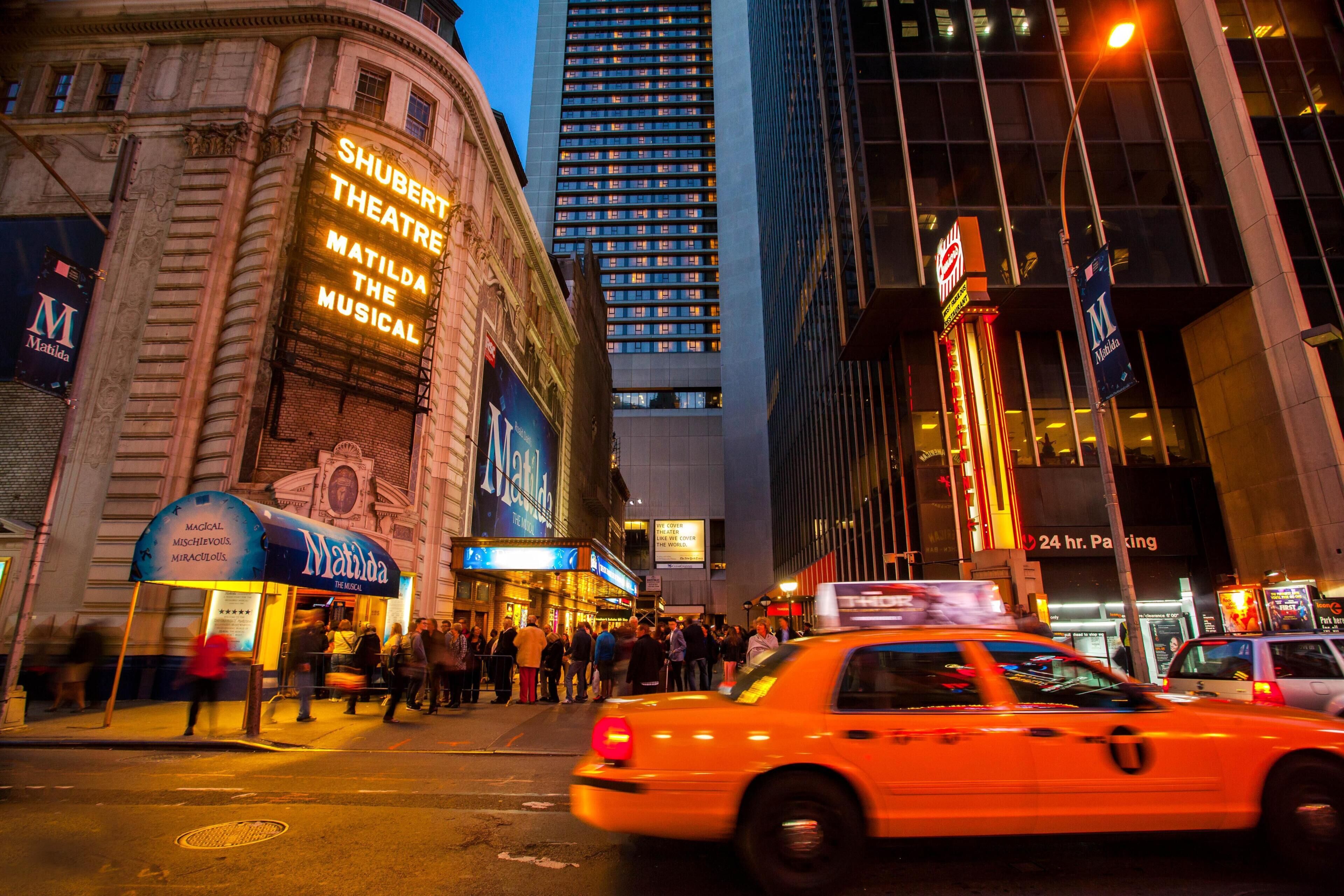 A busy urban street with a prominent theater marquee, a taxi, and tall buildings.