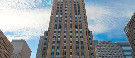 Un edificio alto con una estatua dorada en su fachada, rodeado de otros edificios y banderas.