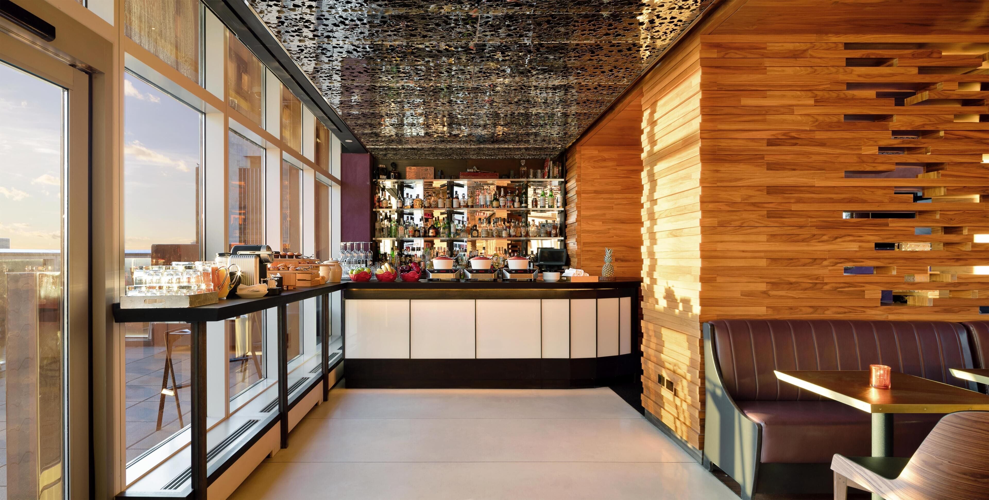 Un área de bar moderna con una pared de madera, una barra con diferentes botellas y asientos.