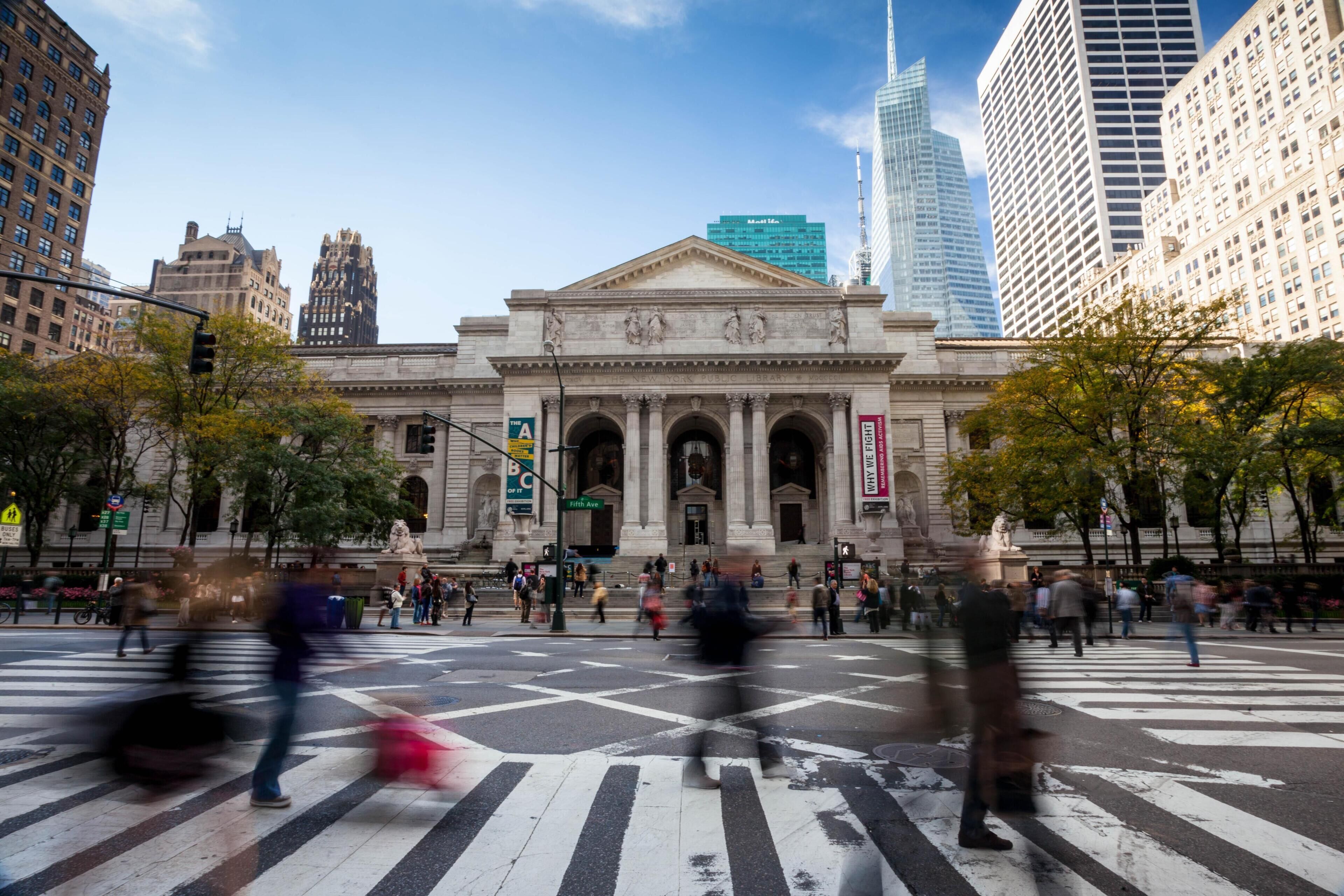 A large public building with classical architecture, including columns and a pediment, surrounded by modern skyscrapers.