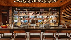A bar with multiple shelves of liquor bottles, a bar counter, and wooden chairs. - Hyatt Centric Times Square New York (New York)