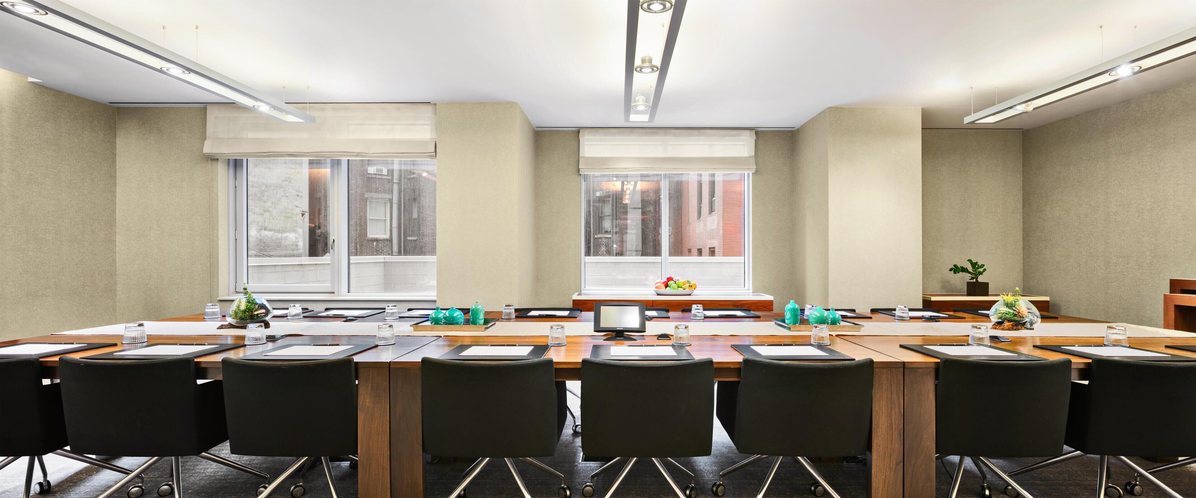 A conference room with a long table, black chairs, a computer, and a window with a view of buildings.