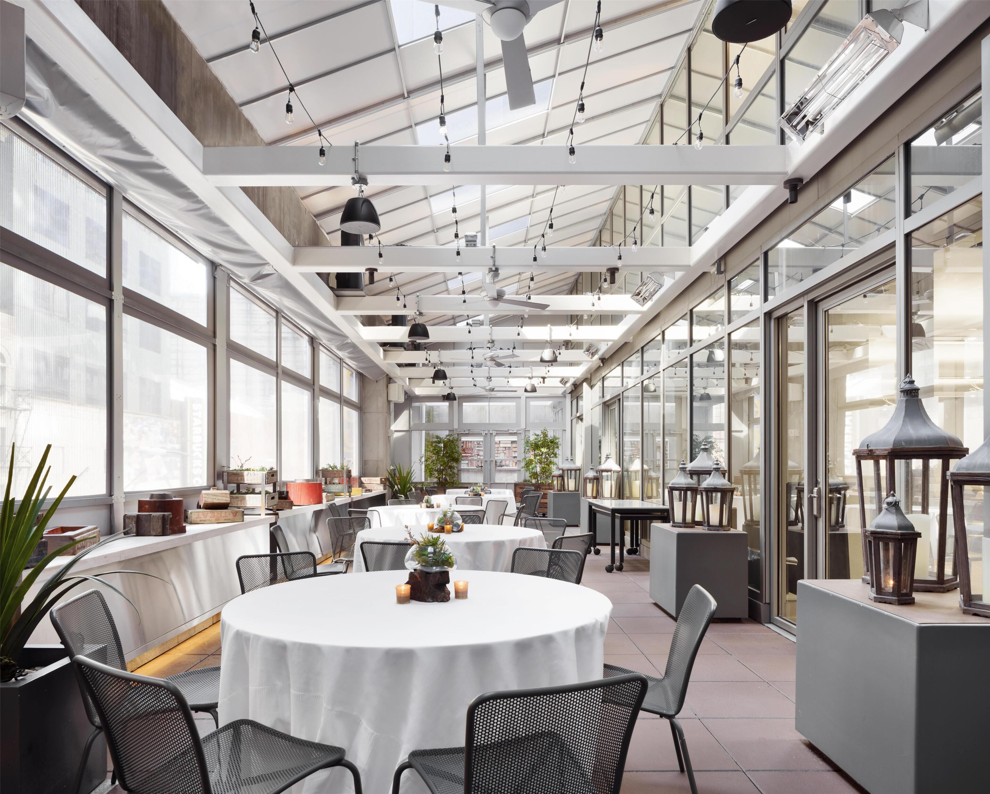 A spacious indoor area with tables and chairs, large windows, and hanging lights.
