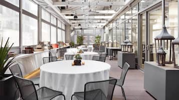 A spacious indoor area with tables and chairs, large windows, and hanging lights.