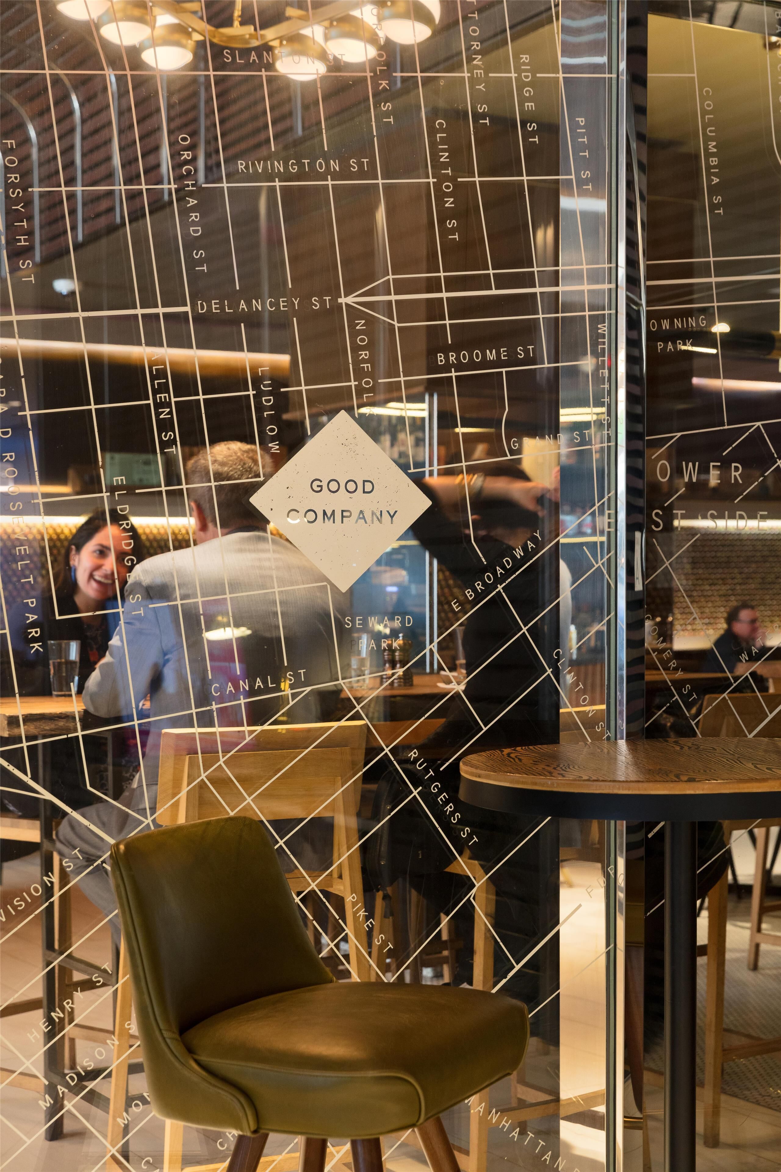 A restaurant with a modern interior, including a glass partition with street names and a sign reading 'GOOD COMPANY.'