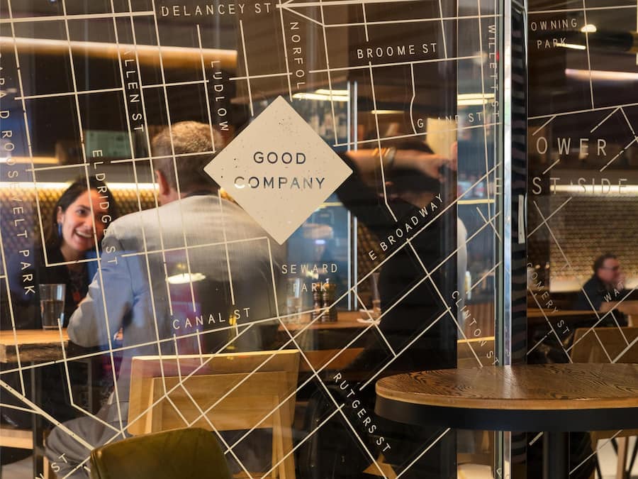 A restaurant with a modern interior, including a glass partition with street names and a sign reading 'GOOD COMPANY.'