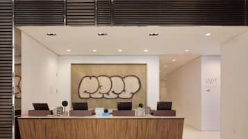 A reception desk with a modern design, a large abstract wall art piece above it, and a sign indicating 'W/C CONCIERGE'.