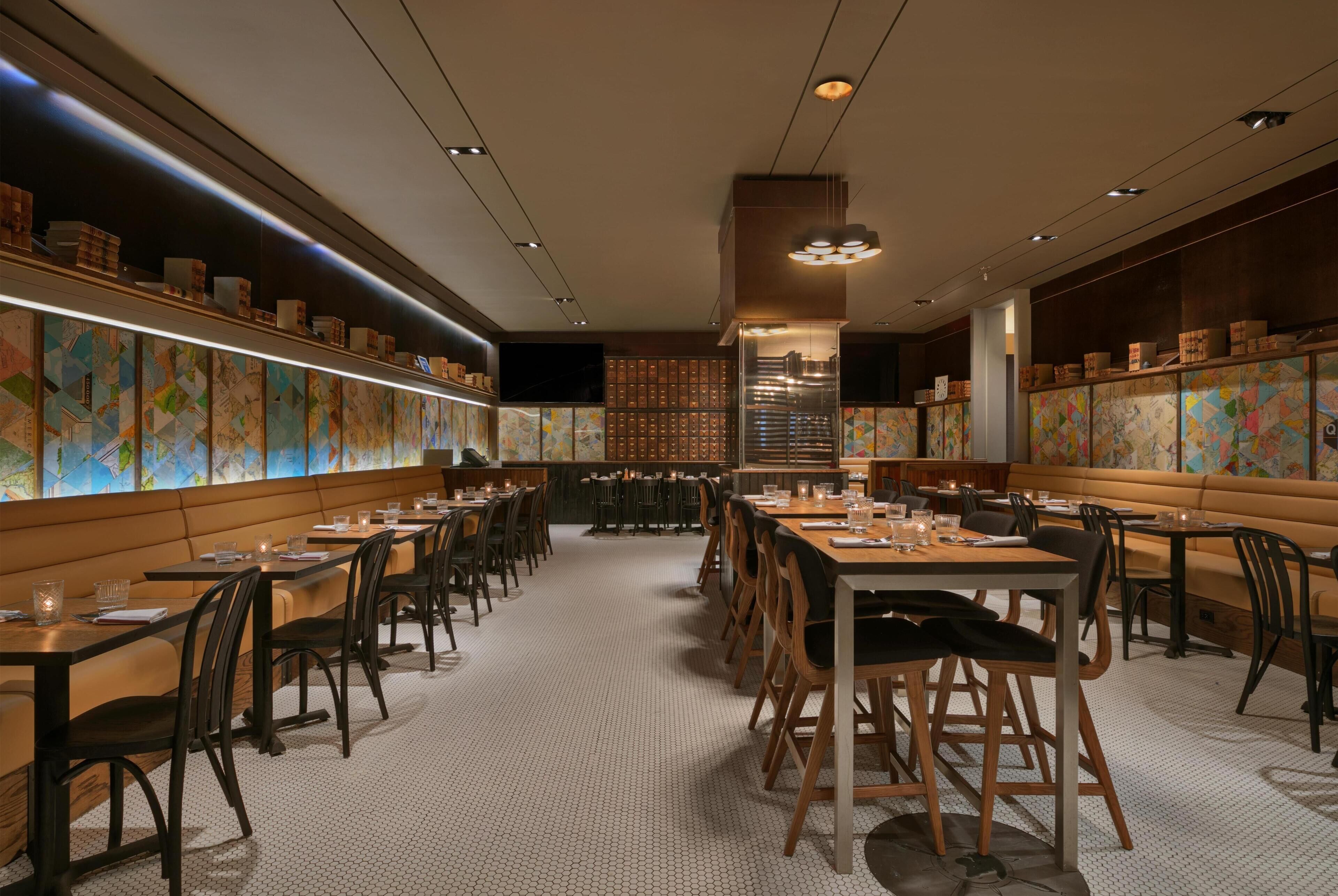 Un restaurante con mesas comunes largas, cabinas individuales y un muro con diseño.
