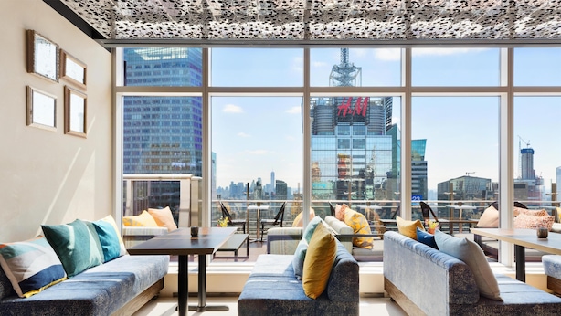 A modern interior with large windows, a city skyline view, and a seating area with sofas and tables. - Hyatt Centric Times Square New York (New York)