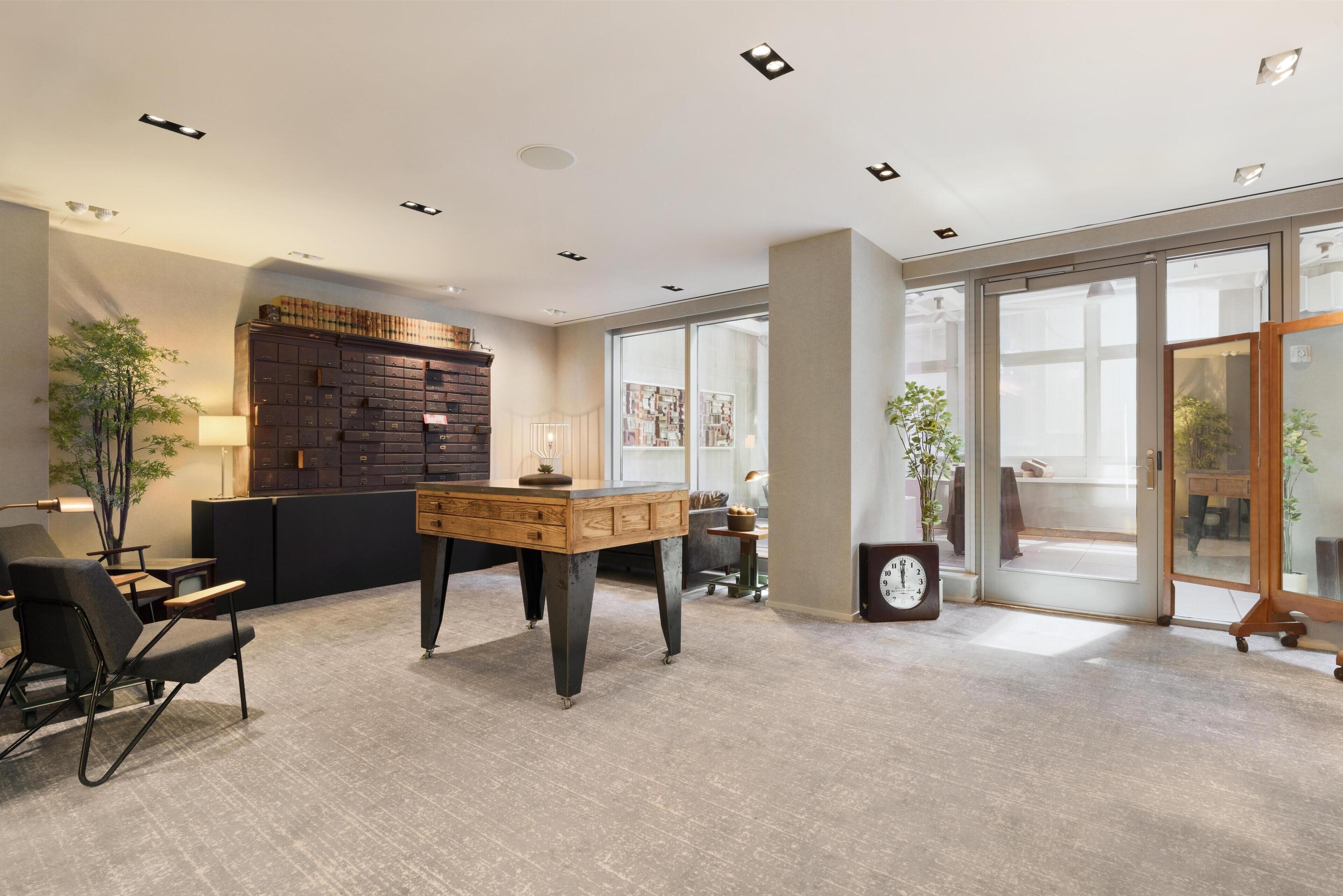 Un espace de bureau moderne comprenant un bureau, des chaises, une bibliothèque et une grande fenêtre.