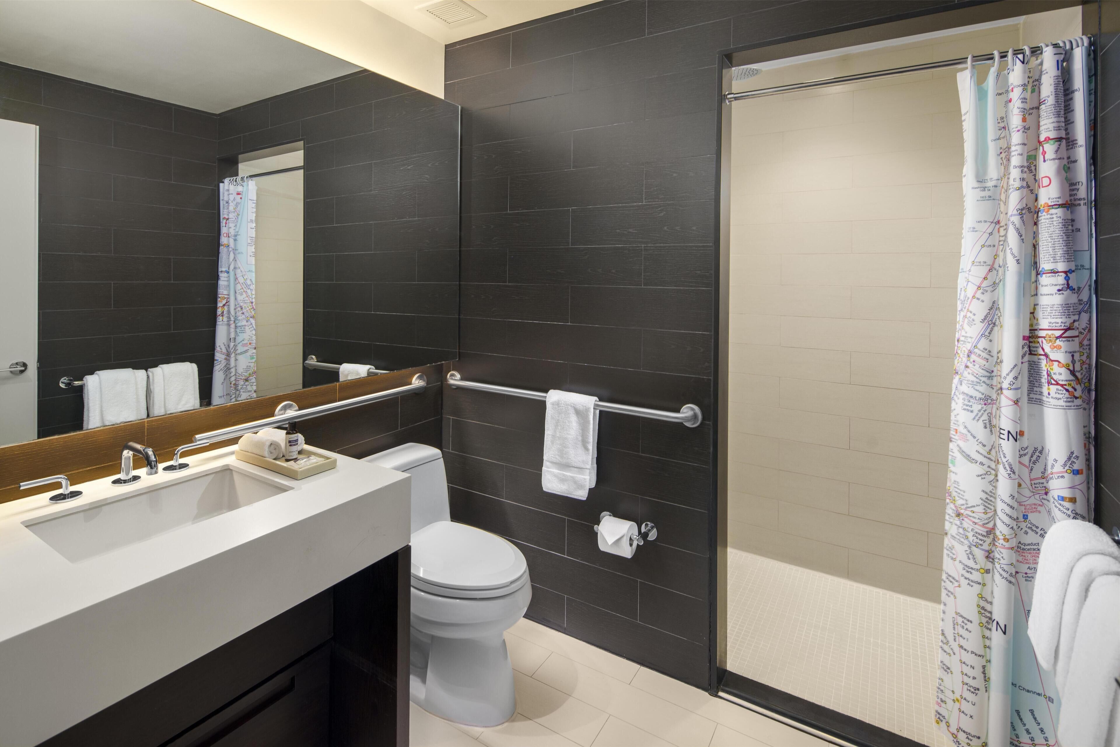 A modern bathroom with a dark tiled wall, a white sink, a toilet, and a shower with a curtain.