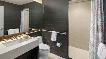 A modern bathroom with a dark tiled wall, a white sink, a toilet, and a shower with a curtain.