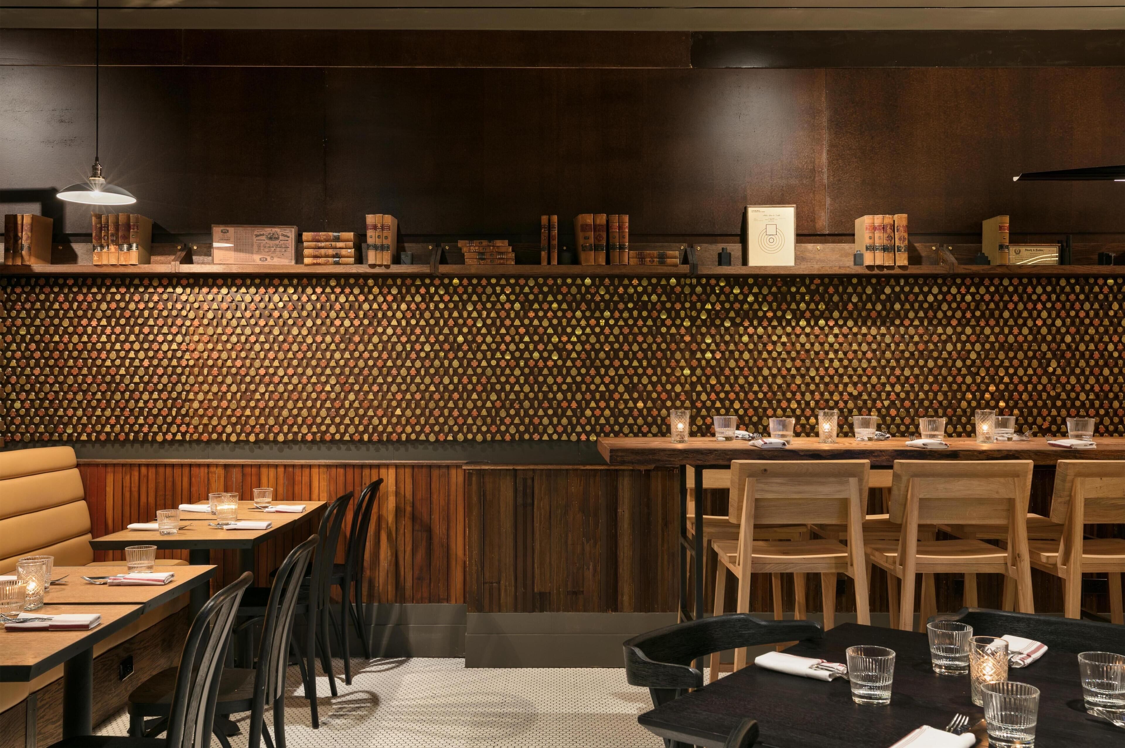 A restaurant interior with wooden panel walls, a bar area with books and glasses, and neatly arranged tables and chairs.