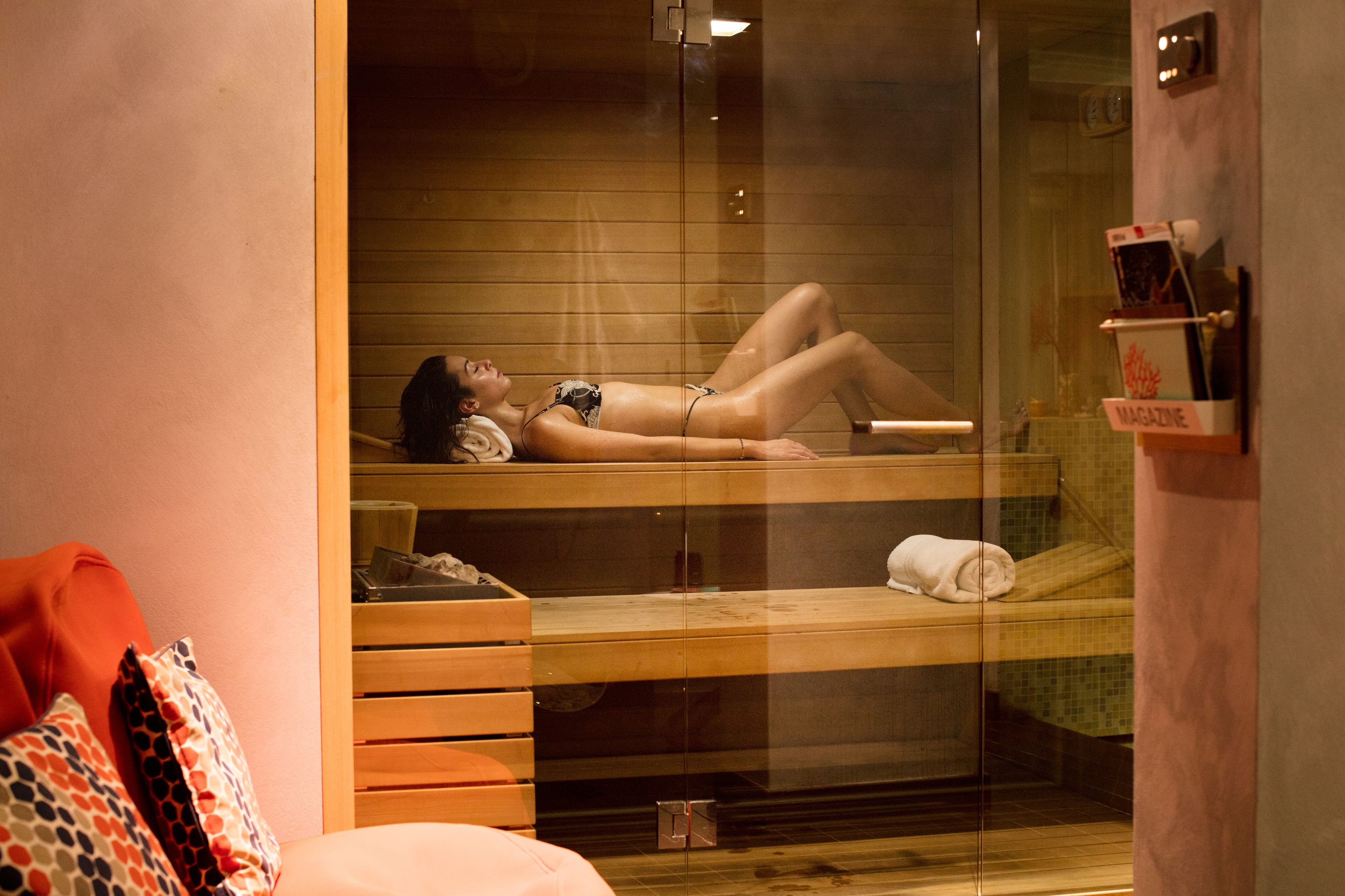 A sauna room with a glass partition, wooden benches, and a magazine rack.