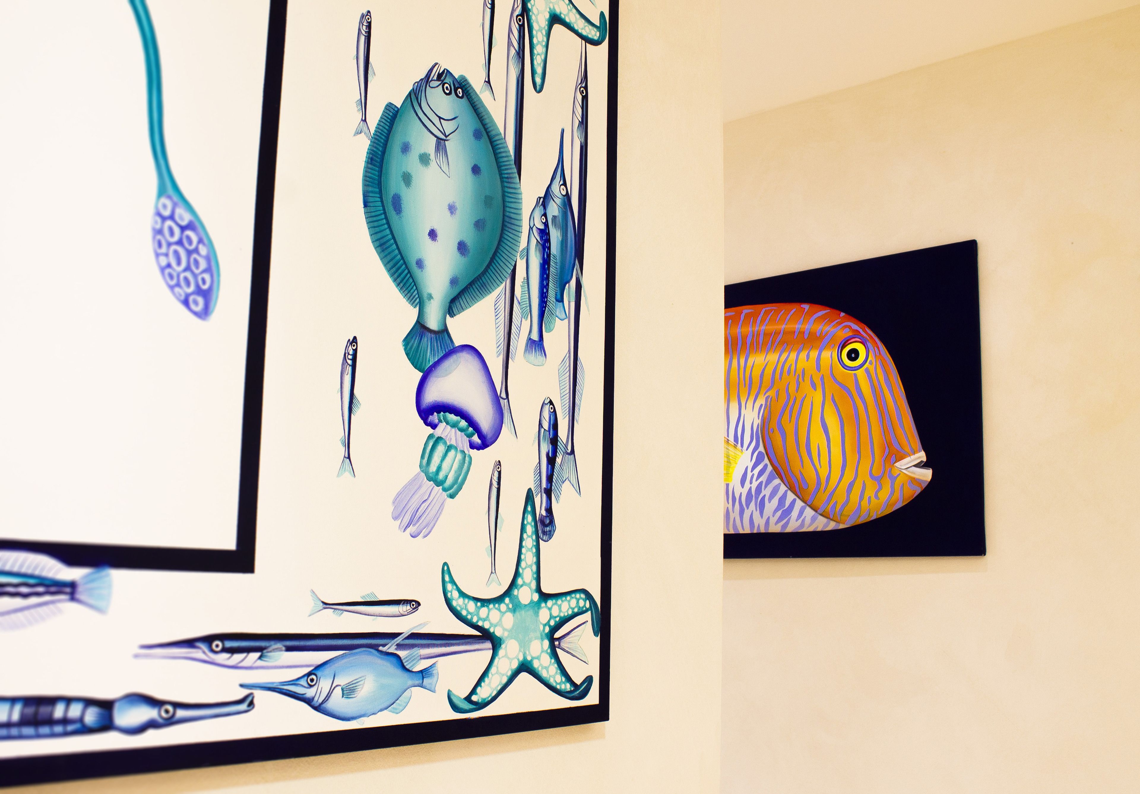 Eine Wand mit zwei gerahmten Kunstwerken: eines zeigt verschiedene Meerestiere, das andere einen stilisierten Fisch.