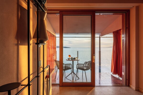 A room with a sliding glass door leading to a balcony with a table and chairs, overlooking a body of water.