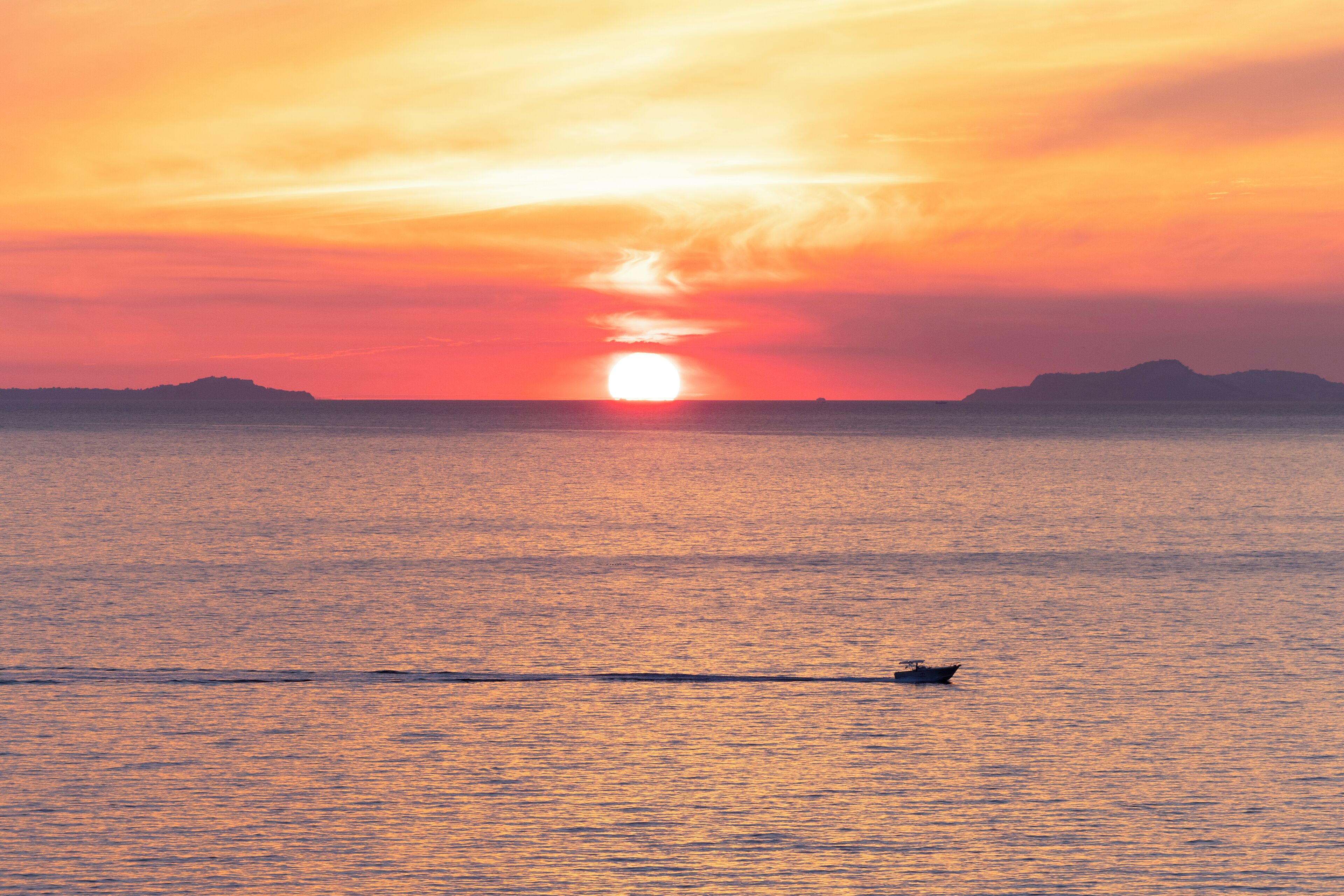 Un atardecer sobre un mar tranquilo con un barco al frente.
