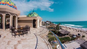A beachside hotel with a dining area, a colorful dome structure, and a view of the ocean.