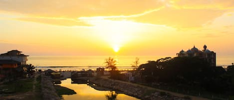 Un atardecer sobre un río tranquilo, con edificios a la izquierda y una gran estructura abovedada a la derecha.