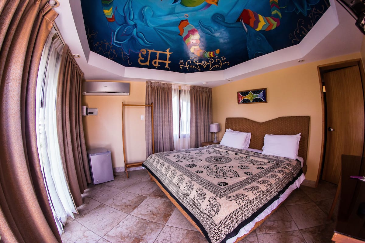 A hotel room with a large bed, a ceiling mural, and a view of the outdoors.