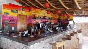 A bar area with a stone counter, wooden stools, and a thatched roof.