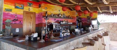 A bar area with a stone counter, wooden stools, and a thatched roof.