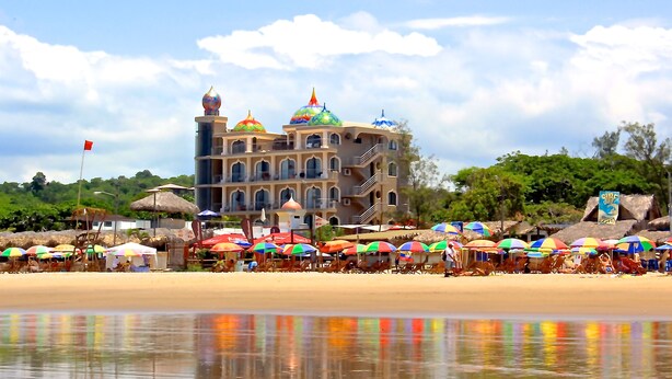 A beachside hotel with multiple colorful umbrellas, a large building with domed roofs, and a clear sky.