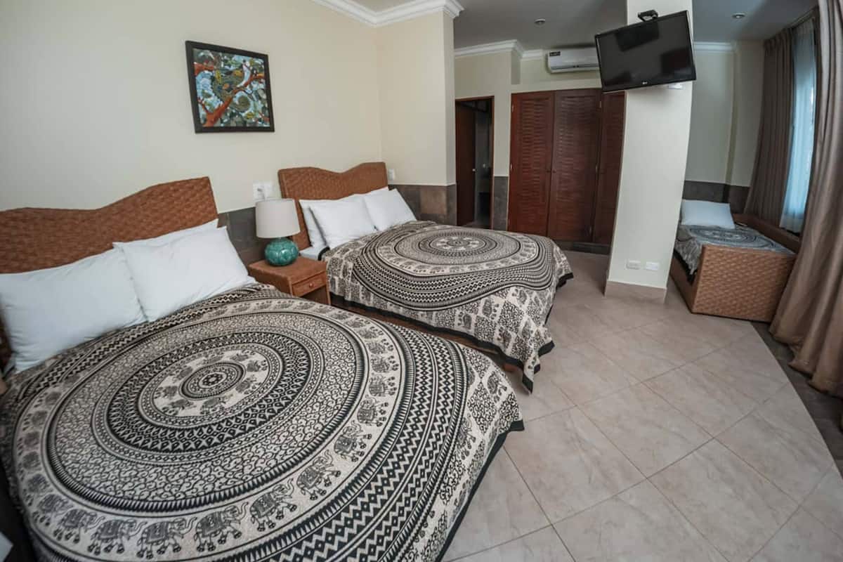 A hotel room with two beds, a TV, a painting, and a wardrobe.