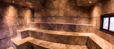 A luxurious bathroom with marble walls and a curved bench.