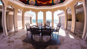 A dining area with a view of the sea, featuring a table with chairs, a ceiling mural, and arched doorways.