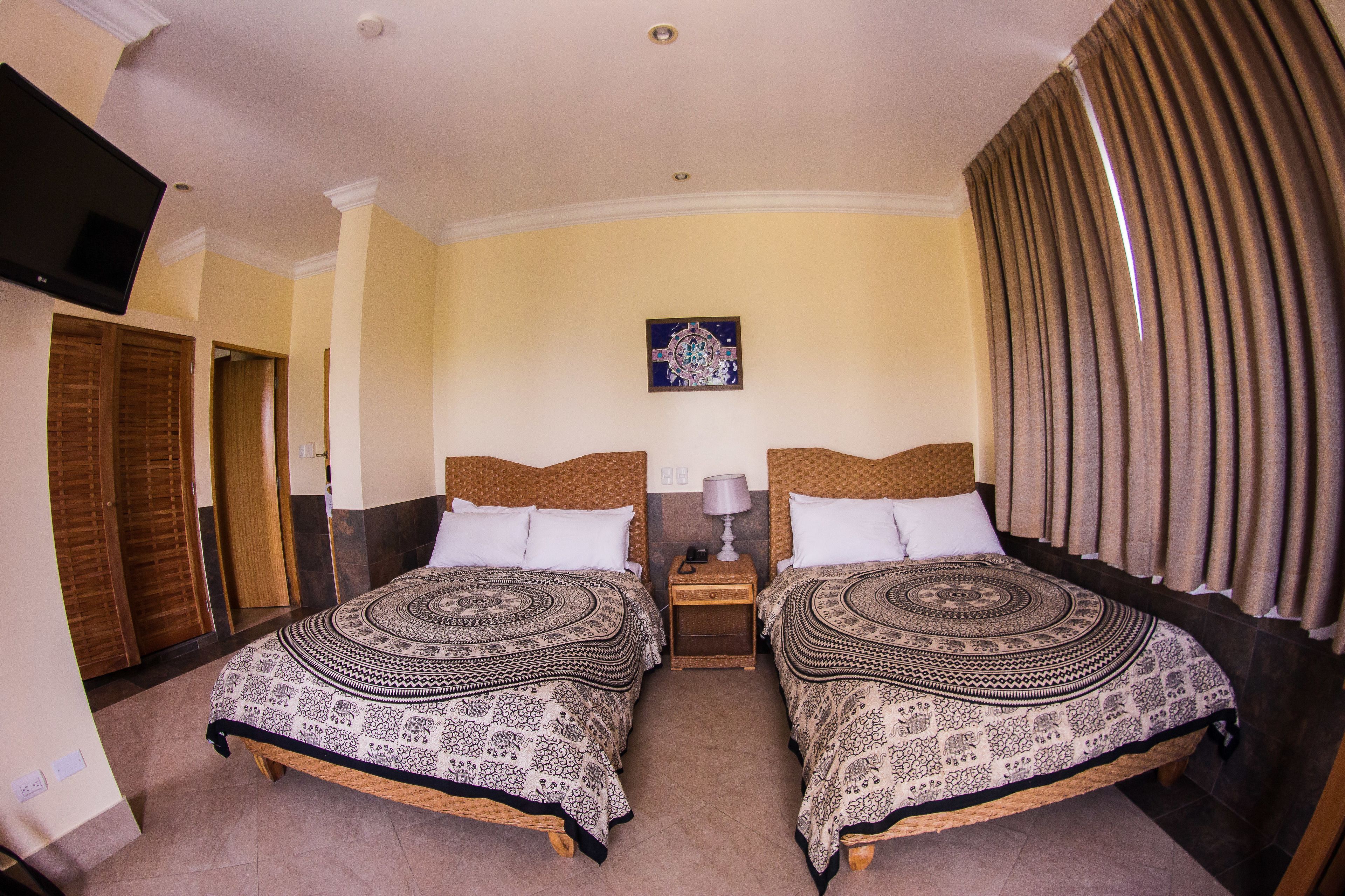 Habitación de hotel con dos camas, un televisor, un cuadro en la pared y una ventana con cortinas.