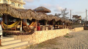A beachfront property with thatched-roof structures, a stone wall, and a sandy beach.
