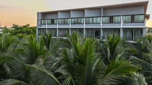 Een modern gebouw met twee verdiepingen, grote ramen en een plat dak, omgeven door weelderige groene palmstruiken.