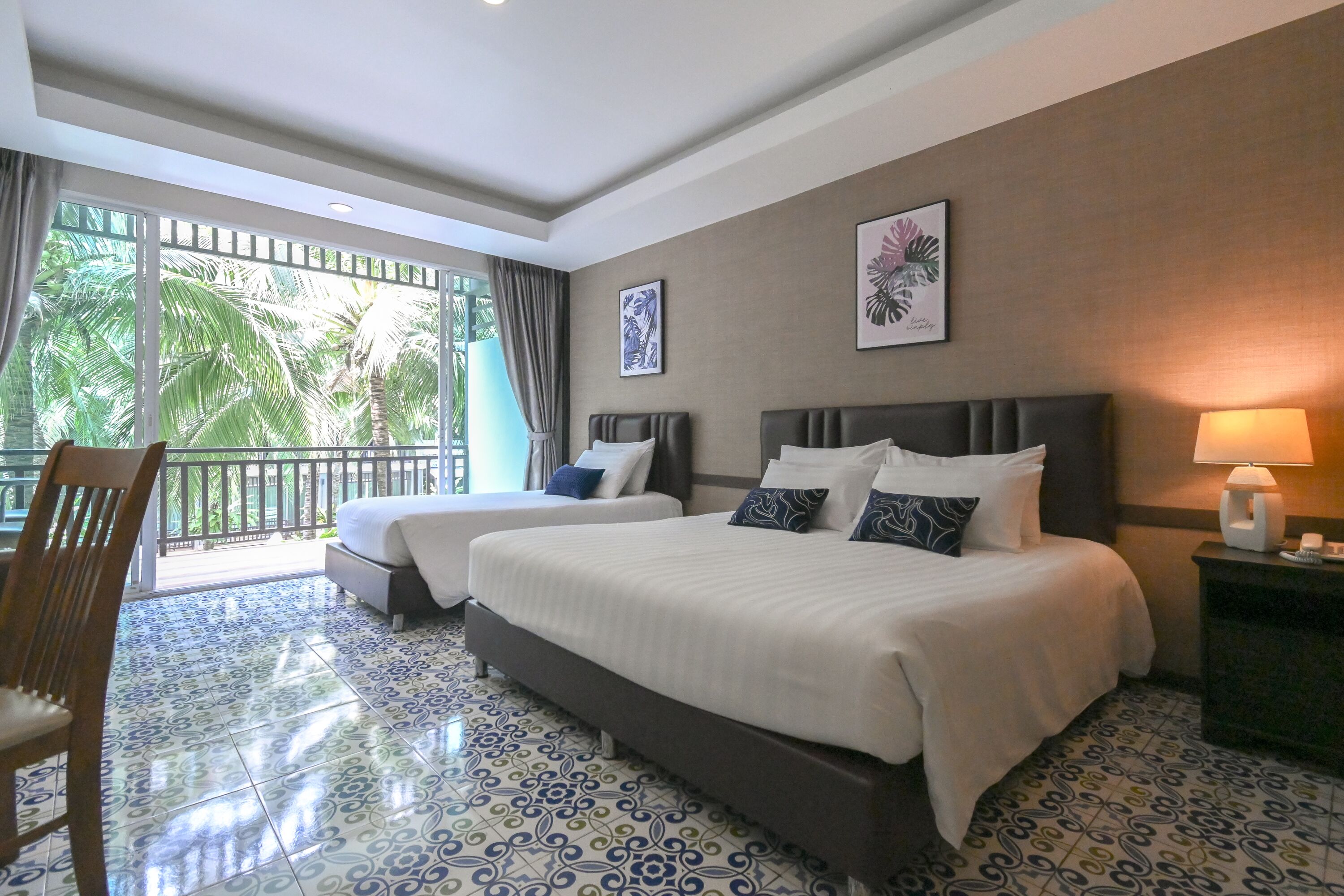 A hotel room with two beds, a balcony with a view of palm trees, and patterned floor tiles.
