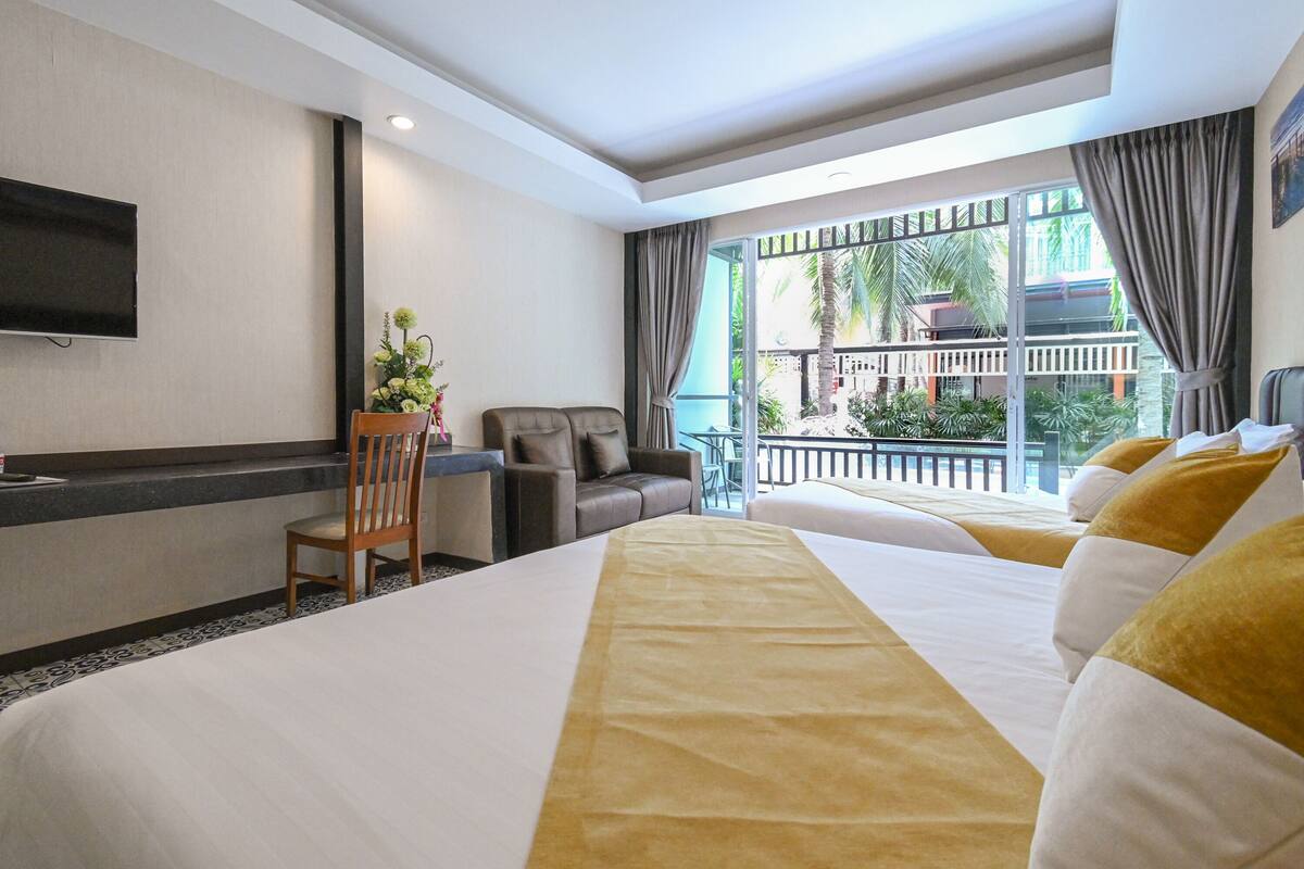 Ein Hotelzimmer mit einem großen Bett, einem Schreibtisch, einem Stuhl, einem Fernseher und einem Balkon mit Pflanzen.