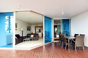 A modern living room with a sofa and coffee table, a dining area with wicker chairs, and a kitchen in the background. - Manta Bargara Resort (Bargara)