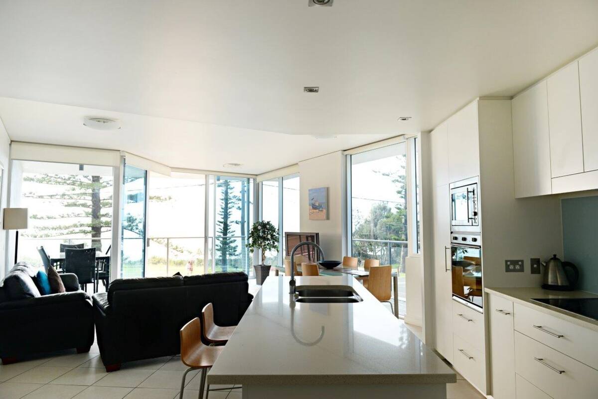 Una cocina moderna con una isla central, ventanas amplias y una zona de comedor con sofá y sillas.