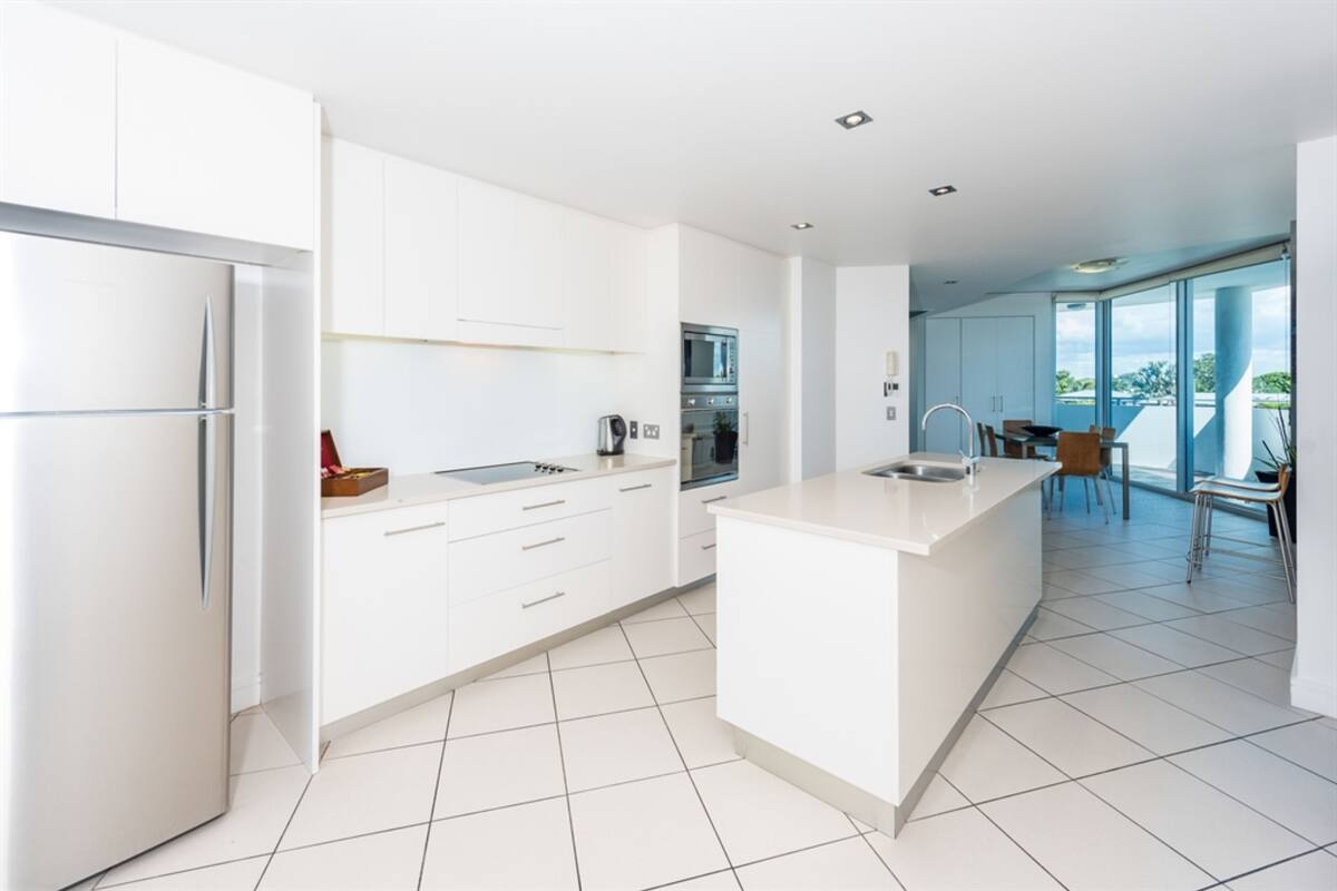 Una cocina moderna con armarios blancos, una isla central y un amplio ventanal con vistas al exterior.