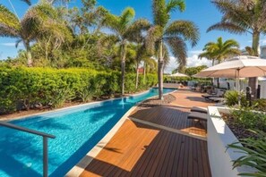 A poolside area with a wooden deck, lounge chairs, and umbrellas. - Manta Bargara Resort (Bargara)
