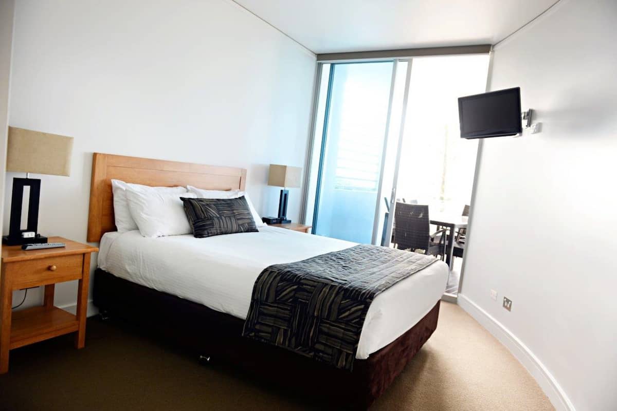 Habitación de hotel con una cama grande, dos mesitas de noche, un televisor de pantalla plana y vistas al exterior.