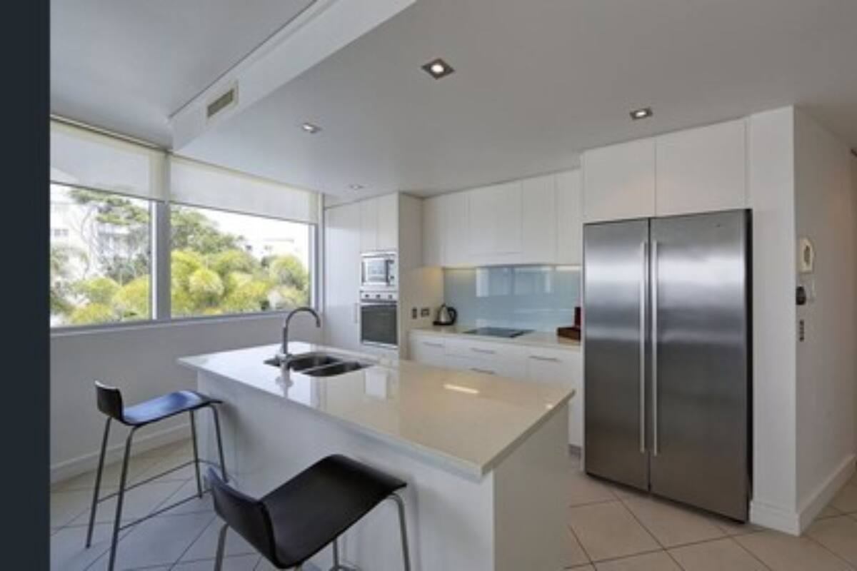 Una cocina moderna con una isla central, electrodomésticos de acero inoxidable y un amplio ventanal que proporciona luz natural.