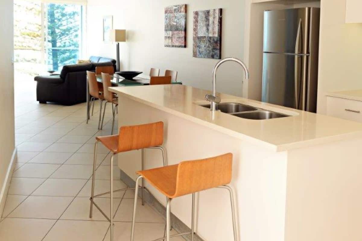 Una cocina moderna con una isla central, taburetes de bar, un refrigerador y un comedor con sofá y sillas.