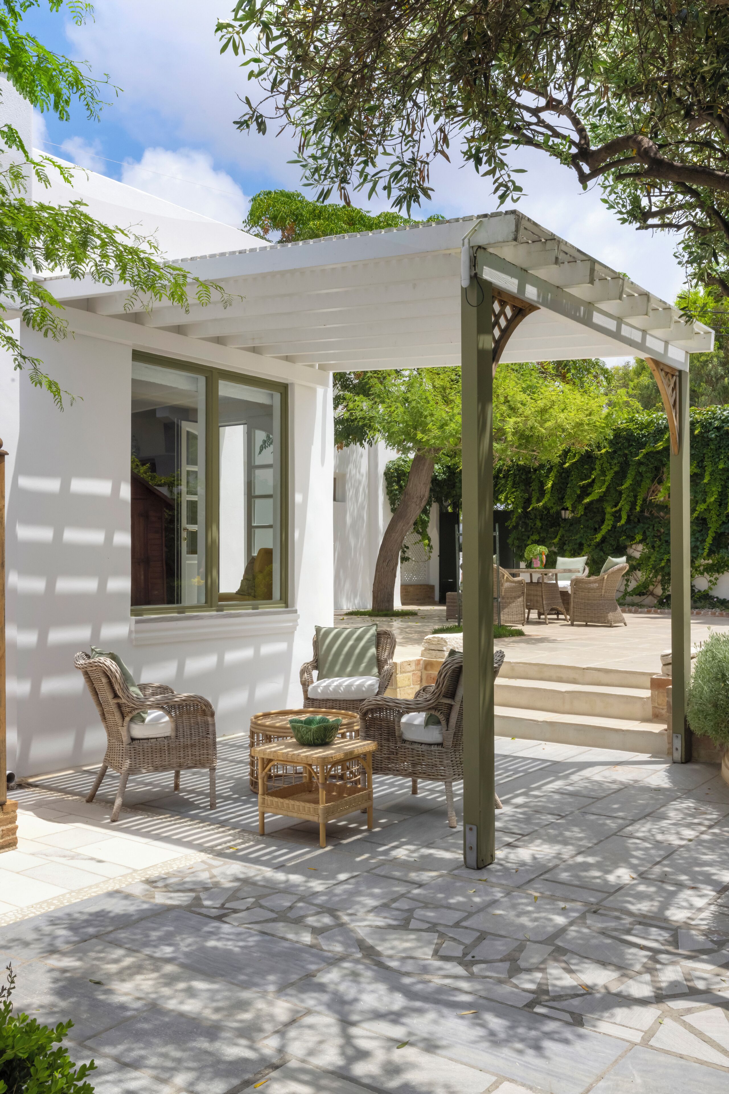 A covered patio with wicker furniture, a stone floor, and a pergola structure.