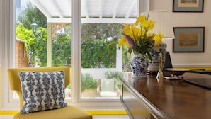 A room with a yellow armchair, a patterned cushion, a vase with yellow flowers, a blue and white vase, and framed pictures on the wall. - Kouneni Apartments (Mykonos)