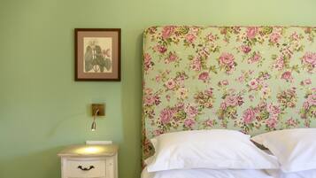A bedroom with a floral-patterned headboard, a bedside table with drawers, and a framed picture on the wall.