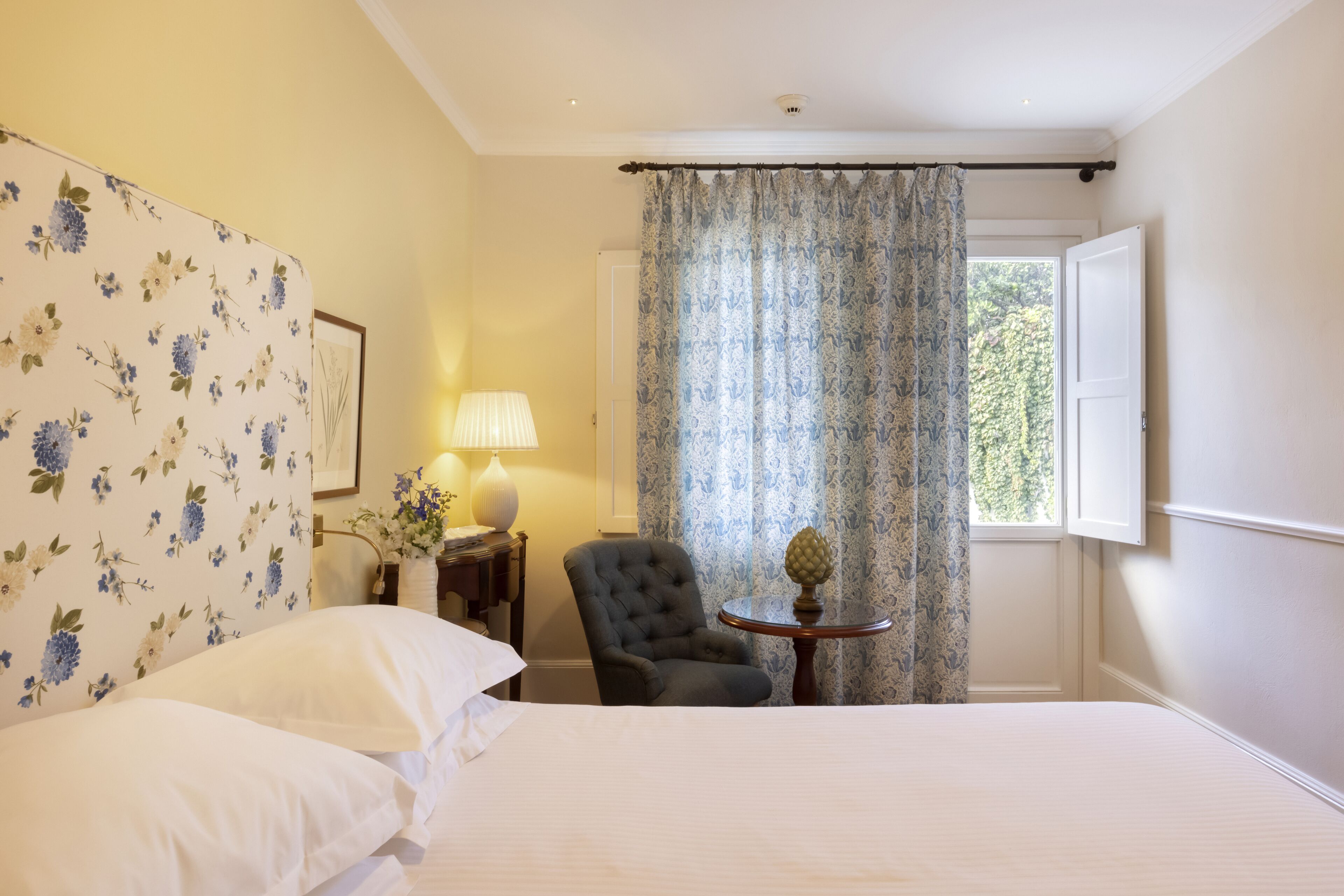 A bedroom with a bed, a chair, a lamp, and a window with curtains.