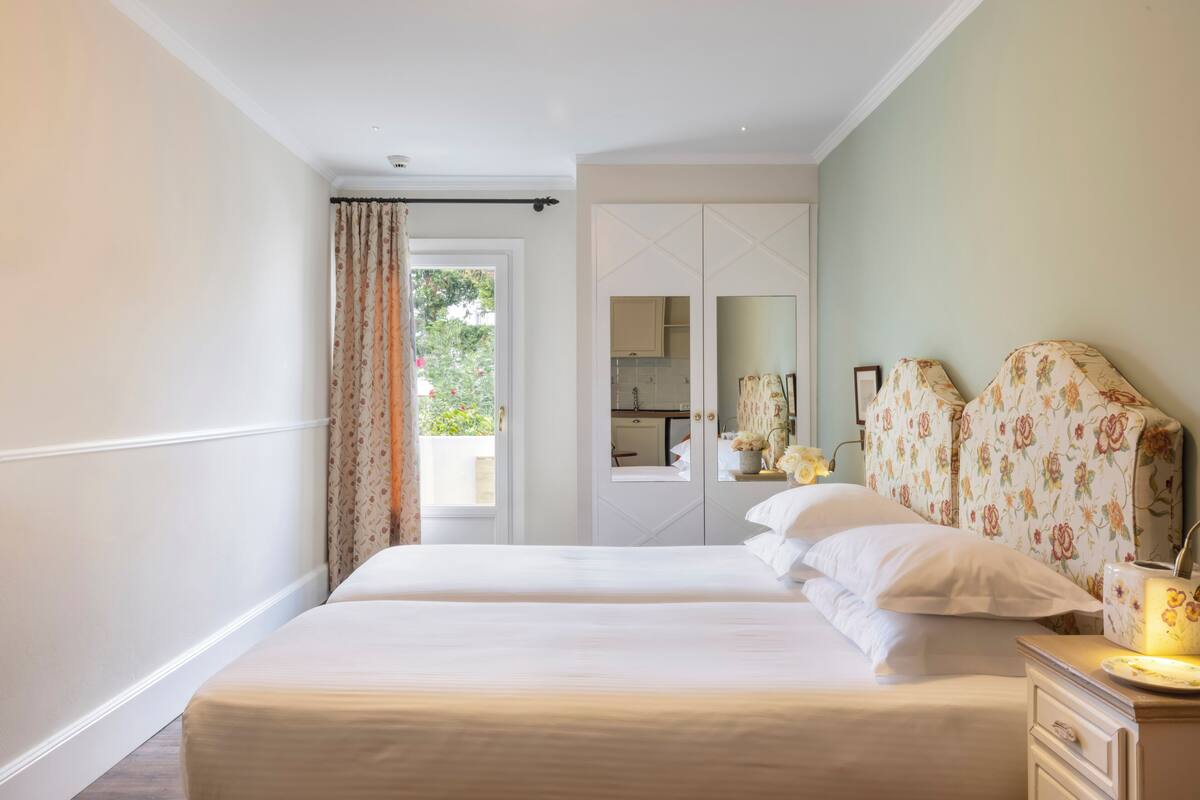 A bedroom with two beds, a dresser, a mirror, and a view of the outdoors.