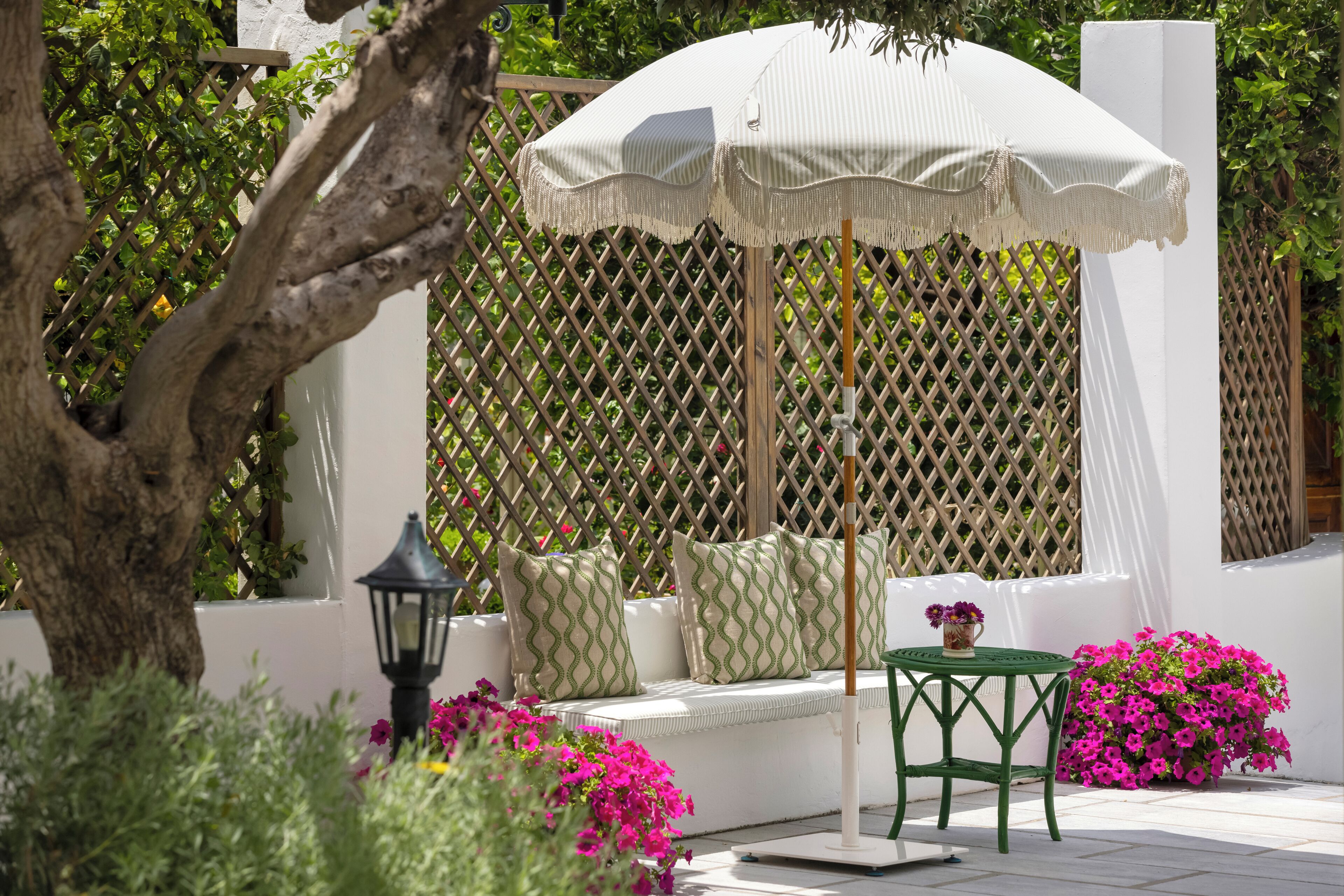 Un espace extérieur aménagé avec des sièges blancs, un parasol blanc, des coussins verts et une petite table sur laquelle est posé un vase de fleurs.
