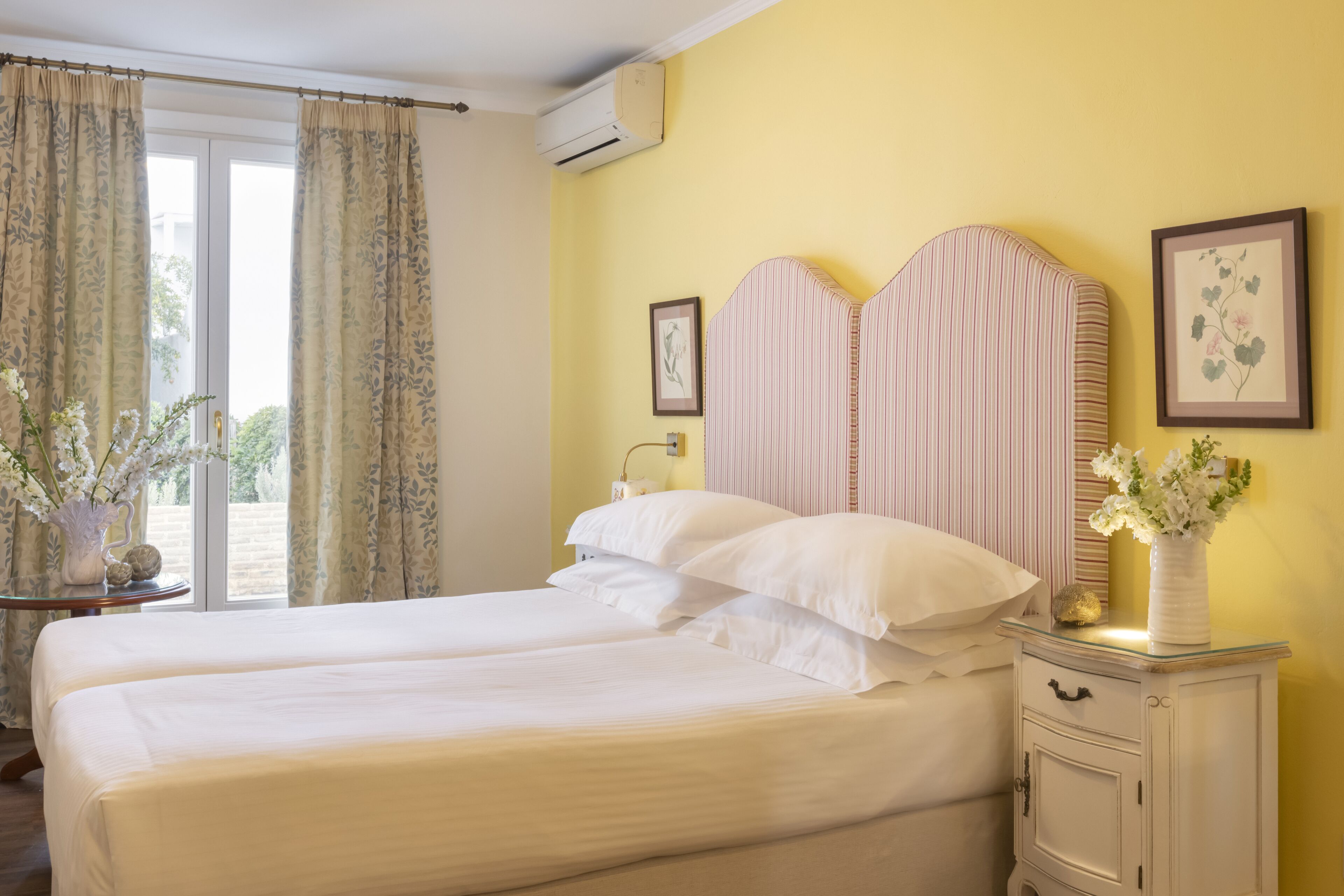 A double bed with white linens, a bedside table with a vase, and a framed picture on the wall.
